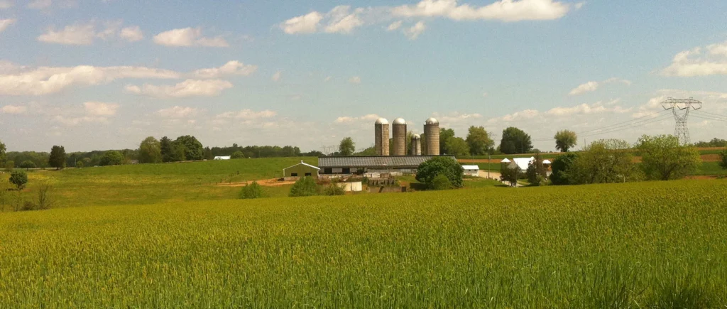 green field with central pa farm in distance under blue sky