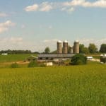 green field with central pa farm in distance under blue sky